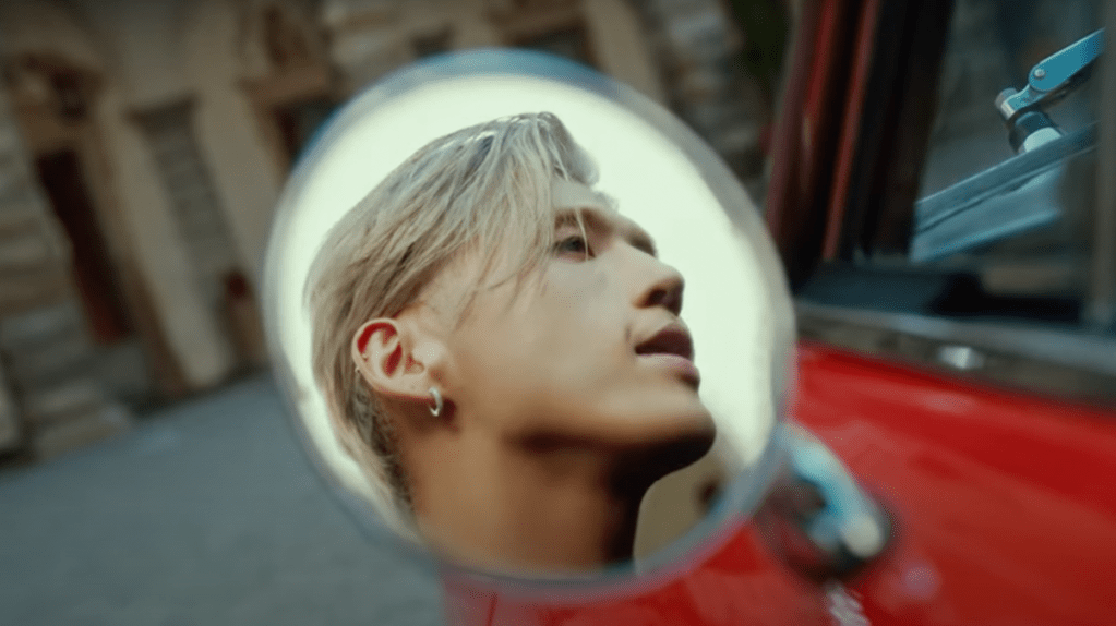 Cena do MV de "Tell My Momma" do KARD com imagem do rosto do BM refletida no espelho do carro