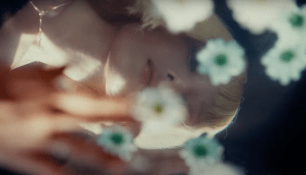 Cena do MV de "Tell My Momma" do KARD com reflexo da silhueta do rosto da Somin na água com flores flutuando