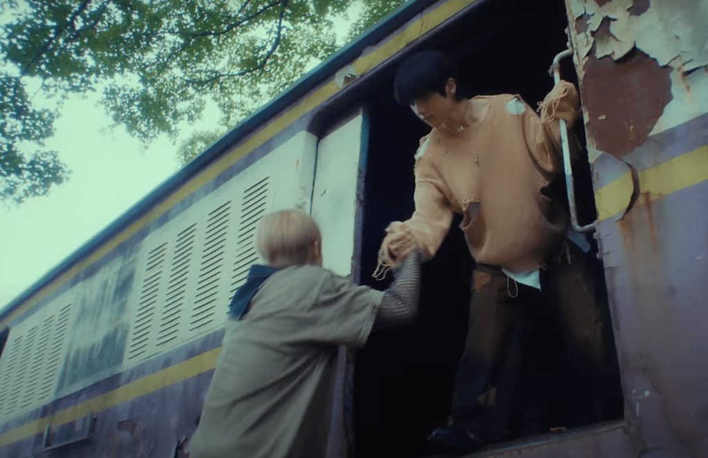Cena do MV de "Rains in Heaven", single em inglês do NCT Dream com cena em um vagão de trem abandonado, enquanto um membro ajuda o outro a subir