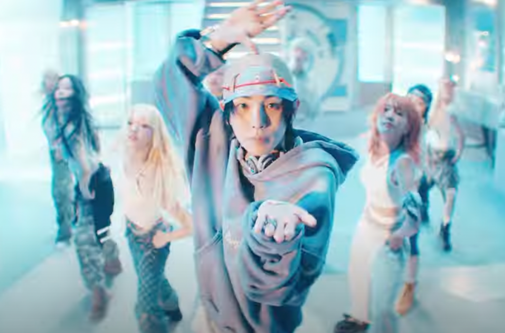 Cena do MV de "Pleasure Shop" com Key no centro dos dançarinos, olhando para a câmera enquanto mexe as mãos