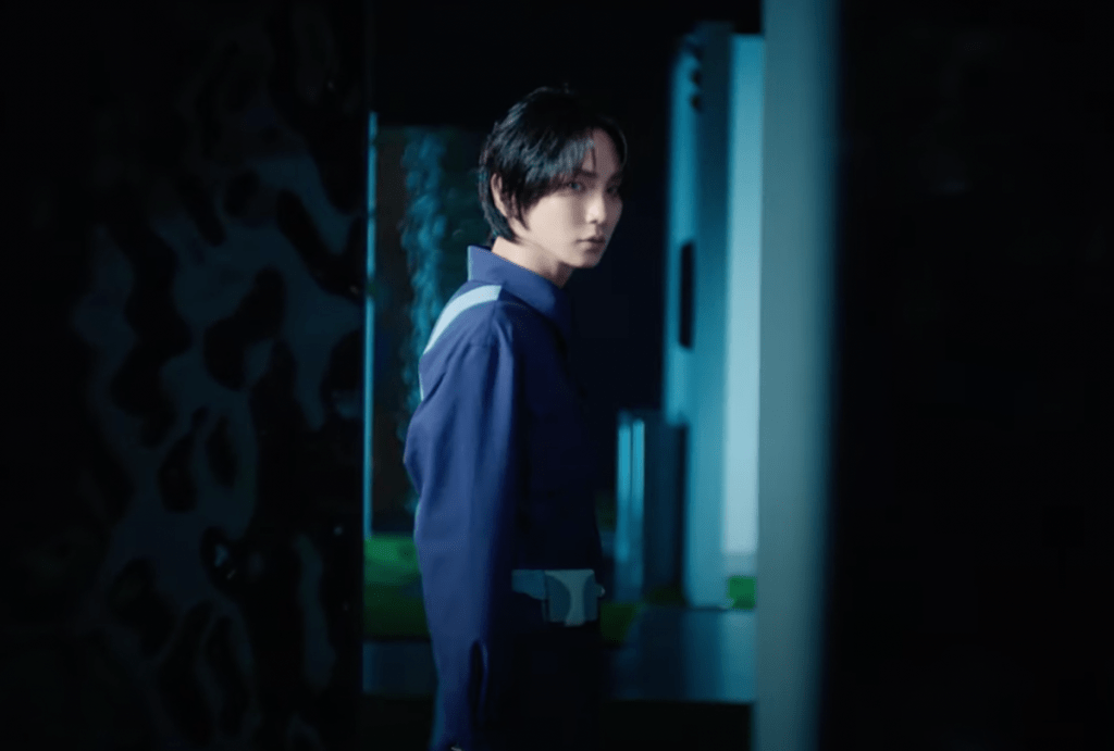 Cena do MV de "Pleasure Shop" com Key em um ambiente escuro, olhando para a câmera