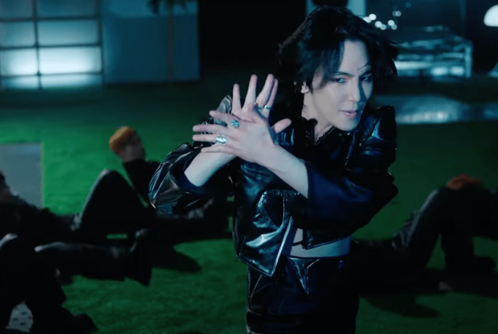 Cena do MV de "Pleasure Shop" com Key de preto, dançando enquanto exala confiança