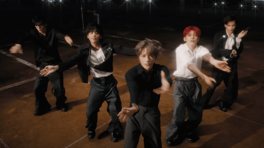 Cena do MV de "Over the Moon" do álbum The Star Chapter: SANCTUARY com todos os membros do TXT dançando em um cenário escuro