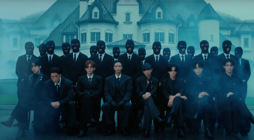 Cena do MV de "Ice On My Teeth" do álbum Golden Hour do ATEEZ com todos os membros vestidos de preto, sentados e cercados por homens com máscara e terno