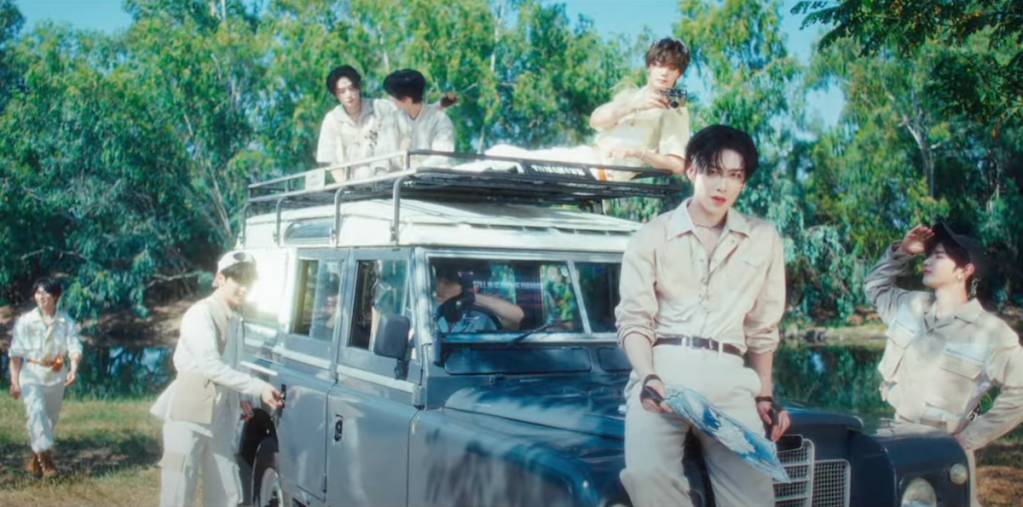 Cena do MV de "BLUE" do álbum Blue Paradise do ZB1. Os meninos estão ao ar livre ao lado de um carro e parecem prontos para se aventurar na natureza