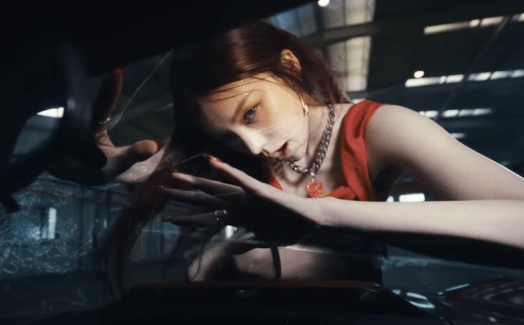Cena do MV de Air do álbum de debut solo da Yeji [Itzy]. Na imagem, ela está em cima do vidro de um carro, olhando para a câmera