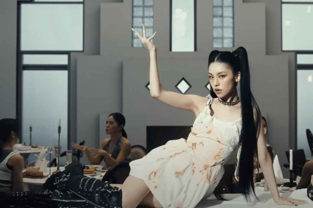 Cena do MV de Air do álbum de debut solo da Yeji [Itzy]. Na imagem, ela está sentada com uma das mãos para cima