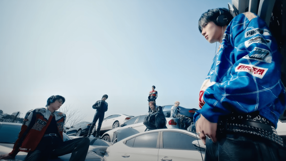 Cena do MV de CHEST, titletrack do álbum JUST ODD do Just B. O grupo aparece em um cenário cheio de carros, usando roupas que parecem de corrida