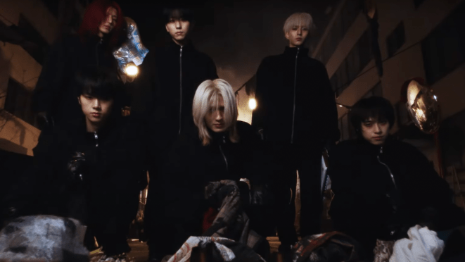 Cena do MV de Beautiful Life com os membros do Xdinary Heroes vestidos de preto em um cenário caótico e escuro