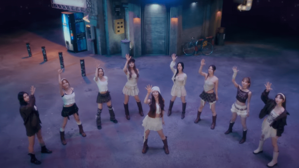 Cena do MV de LOVE LINE do NiziU com todas as integrantes com as mãos para cima em um espaço aberto