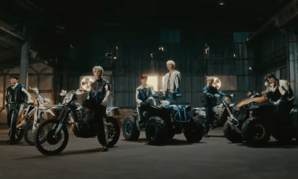 Cena do MV de LOVE RACE com os membros do SF9 ao lado de motos, olhando para a câmera