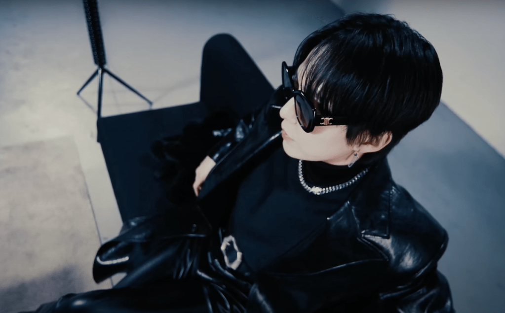 Cena do MV de WHEE! do álbum Interview X do Xiumin. Na imagem, ele aparece de preto e com óculos escuro