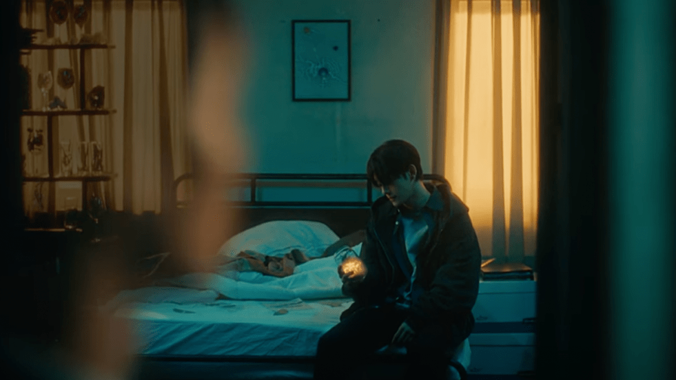 Cena do MV de Broken Party, novo single do Chen do EXO. Ele aparece ao fundo, sentado na cama, em um quarto escuro