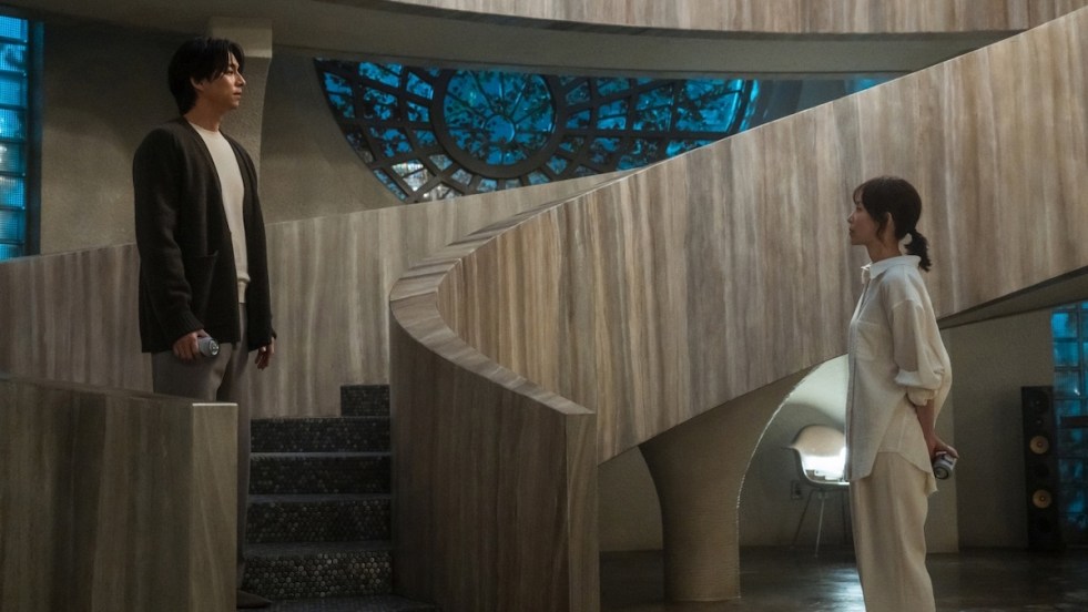 Cena do K-Drama The Trunk com Gong Yoo e Seo Hyun-Jin olhando um para o outro em uma casa grande cinza e com uma escada em caracol