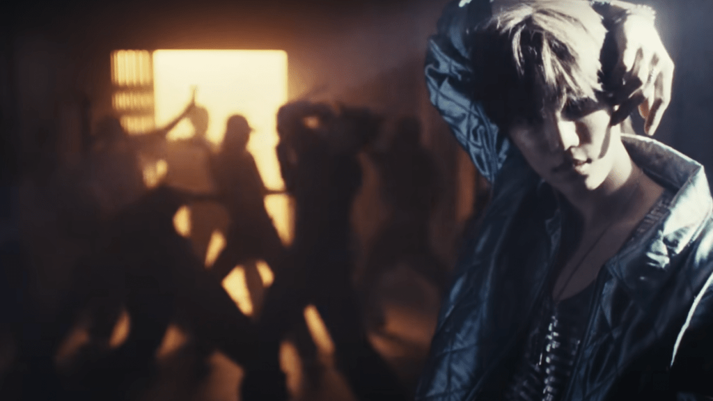 Cena do MV de Wait On Me do novo álbum do Kai com mesmo nome. Ele aparece no canto direito da tela com silhuetas de dançarinos ao fundo