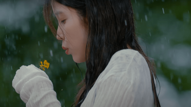Cena do MV de "Never Ending Story" do álbum A Flower Bookmark, Pt. 3 da IU. Na imagem, ela aparece segurando uma flor amarela no meio da chuva