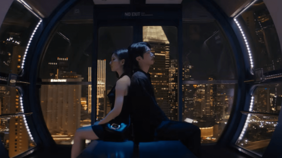 Cena do MV de "Don't Say You Love Me" do álbum Echo com Jin (BTS) e a atriz Shin Se-kyung sentados um de costas para o outro com o cenário noturno da cidade ao fundo