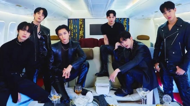 Imagem com os seis membros do Monsta X vestidos de preto em um cenário claro com uma mesa cheia de taças