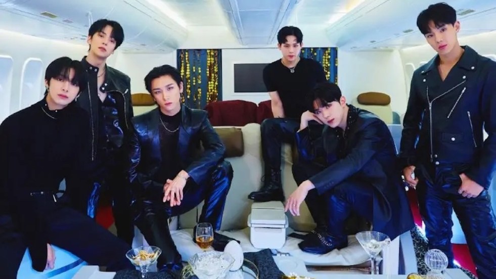 Imagem com os seis membros do Monsta X vestidos de preto em um cenário claro com uma mesa cheia de taças