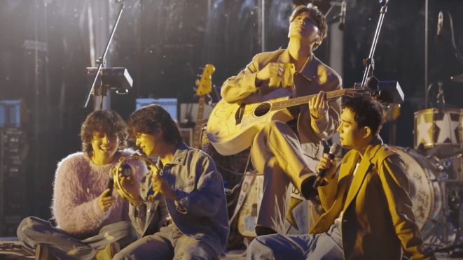 Cena do vídeo especial de performance do The Rose para o lançamento do álbum WRLD. Woosung, Hajoon, Jaehyung e Dojoon estão sentados no palco em um lugar cercado pela natureza durante a noite