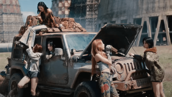 Cena do MV de "Girls Will Be Girls" do ITZY. Na imagem, as meninas estão em um Jeep em um cenário pós-apocalíptico