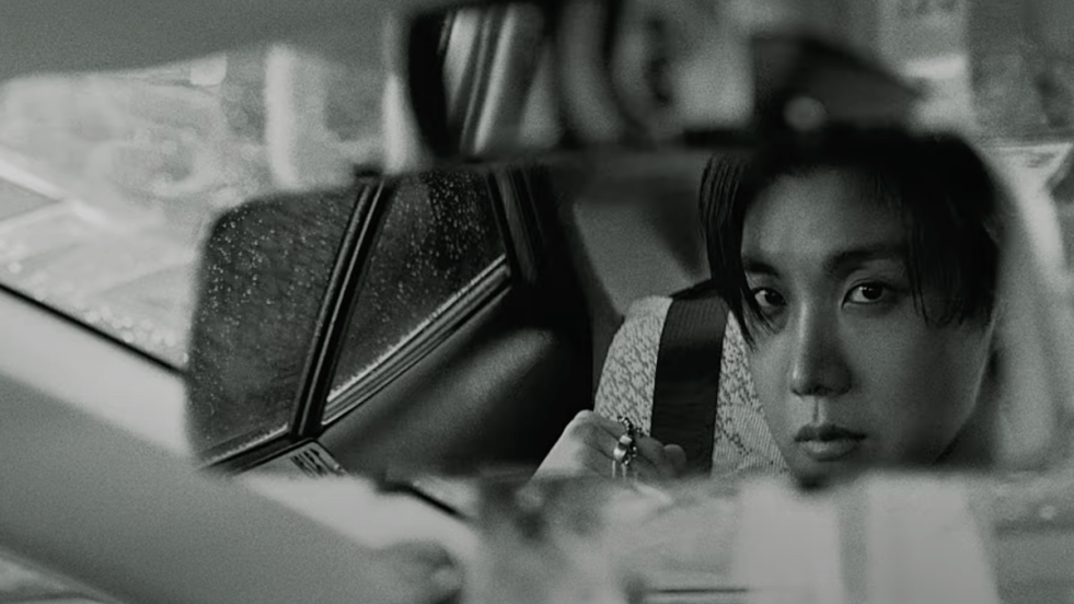 Cena do MV de "Killin' It Girl" do J-Hope em parceria com GloRilla. Na imagem, ele olha sua imagem refletida no espelho do carro