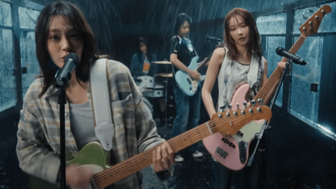 Cena do MV de "Dear (눈물참기)" do álbum In a Million Noises, I'll Be Your Harmony do QWER. Na imagem, as quatro integrantes cantam e tocam embaixo de chuva