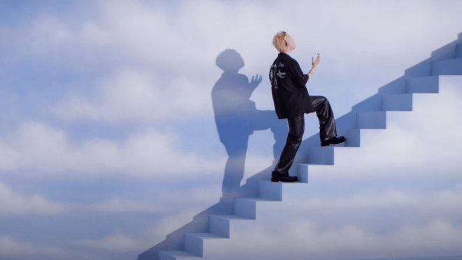 Cena do MV de "SING ALONG!" do álbum BLISS do Doh Kyung Soo [EXO]. Na imagem, ele sobe uma escada com um fundo que lembra o céu com nuvens