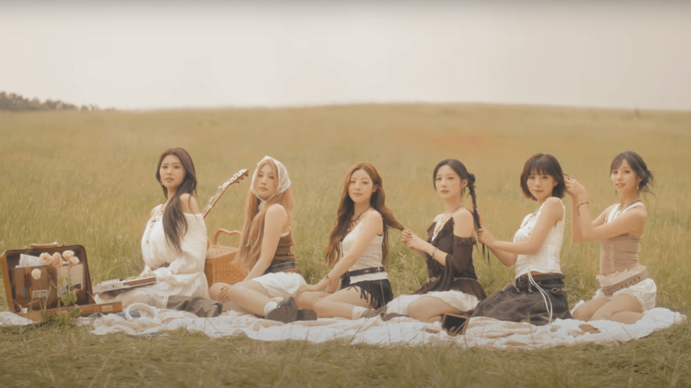 Cena do MV de "DOREMI" do álbum I Miss My... com todas as integrantes do PURPLE KISS sentadas na grama, uma atrás da outra, em um cenário ao ar livre