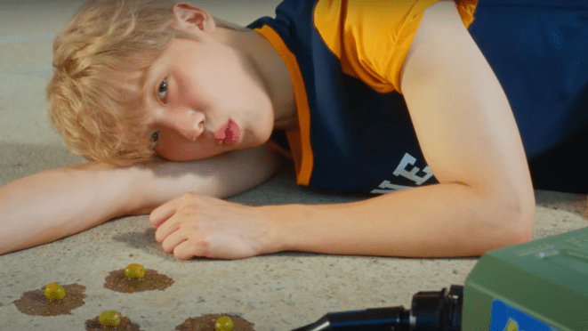 Cena do MV de "EXTRA VIRGIN" do álbum CHAMELEON. Sanha aparece deitado no chão, com azeitonas e azeite de oliva