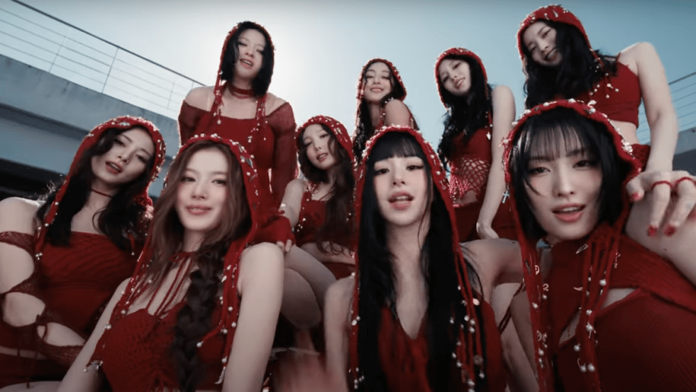 Cena do MV de "THIS IS FOR" do TWICE, com todas vestidas de vermelho, olhando para a câmera