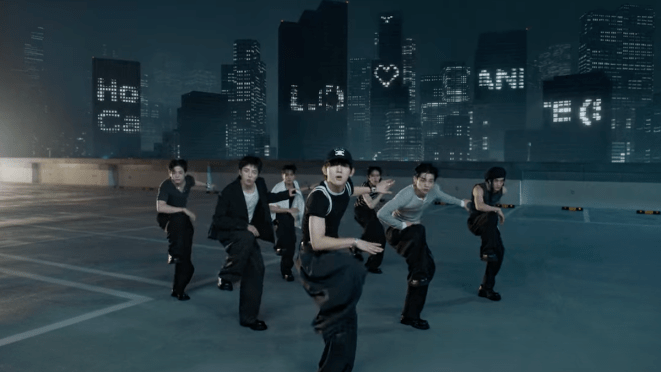 Cena do MV de "How Can I Do" do álbum LOVE ANECDOTE(S) do EVNNE, com todos os membros dançando em um cenário noturno e desenhos iluminados nos prédios ao fundo