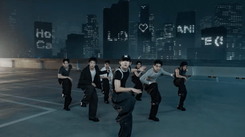 Cena do MV de "How Can I Do" do álbum LOVE ANECDOTE(S) do EVNNE, com todos os membros dançando em um cenário noturno e desenhos iluminados nos prédios ao fundo