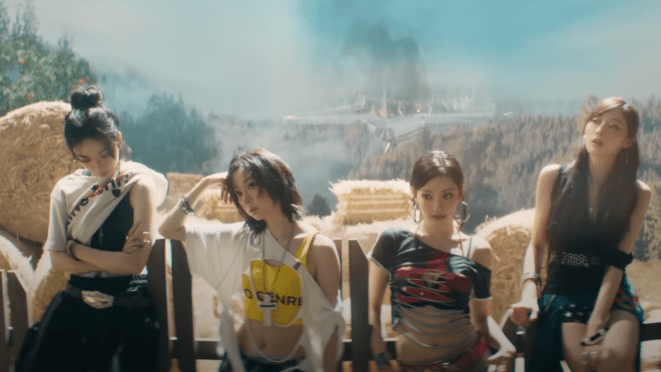 Cena do MV de "Rich Man" com Karina, Winter, Ningning e Giselle em um cenário que lembra uma fazenda, com a fumaça de uma fábrica ao fundo