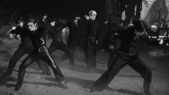 Cena do MV de "Ash" do álbum Ashes to Light to ATEEZ. Vestidos de preto, os membros dançam em um cenário escuro
