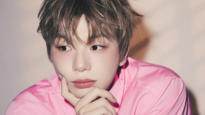 Imagem de close do Kang Daniel pensativo, vestindo uma camisa rosa