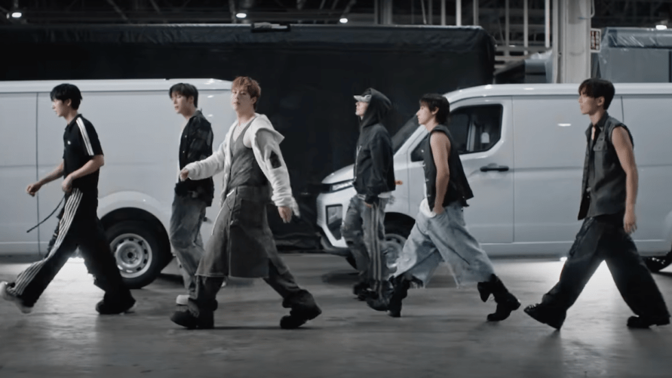 Cena do MV de "N the Front" do álbum THE X do Monsta X com os seis caminhado em um espaço que parece um grandee galpão