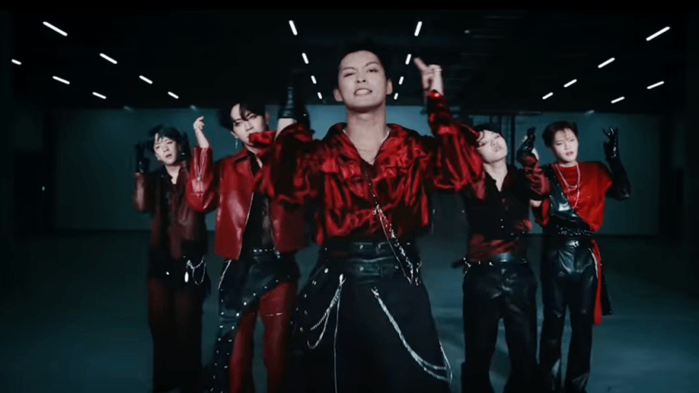 Cena do MV de "TOO LOUD" do álbum ROAR do ORβIT com todos os integrantes de vermelho e preto em um momento de pose da coreografia