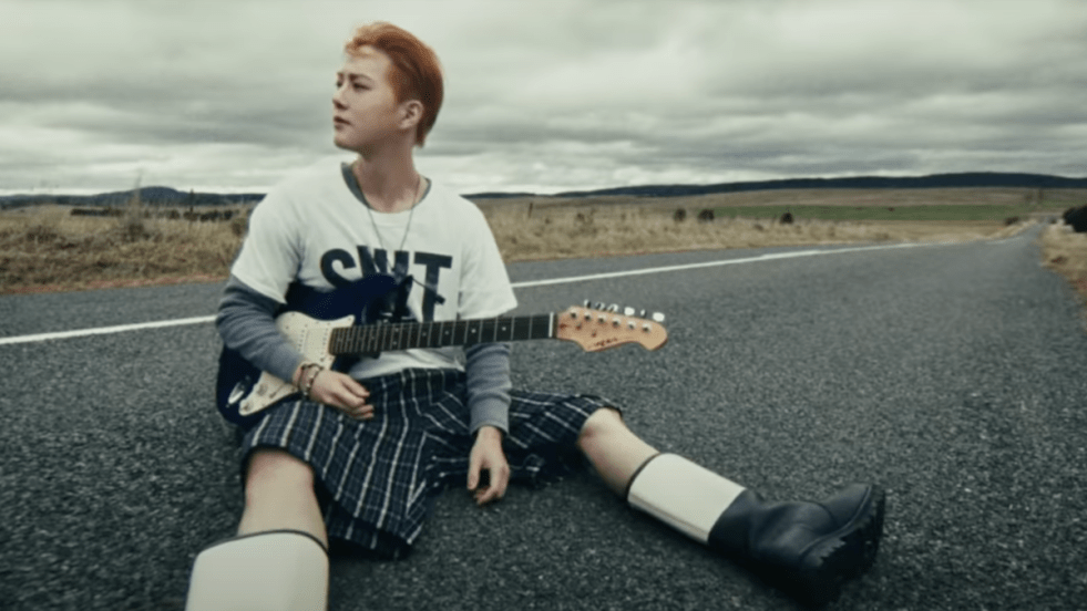 Cena inicial do MV de Who Are You do Suho [EXO sentado no meio da estrada, com uma guitarra no colo