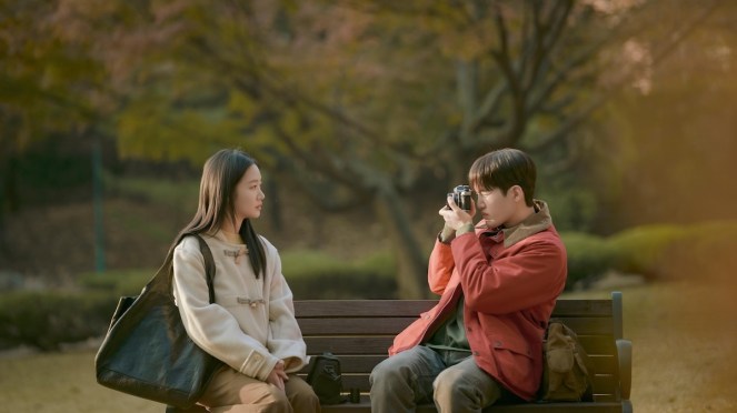 K-Drama You and Everything Else com Kim Go-Eun (Ryu Eun-Jung) e  Kim Gun-Woo (Kim Sang-Hak) sentados no banco de um parque enquanto ele tira uma foto dela