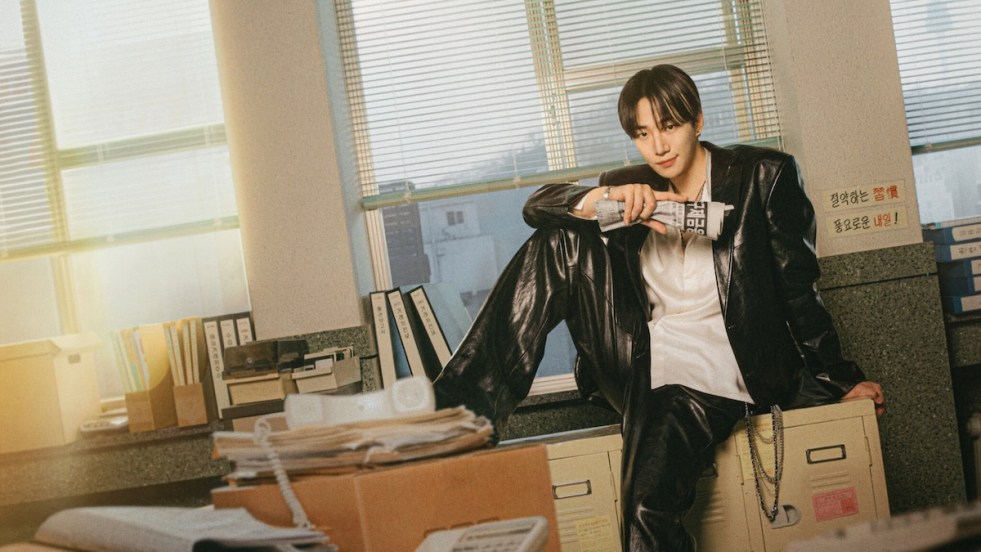 Imagem do K-Drama Typhoon Family com Kee Junho sentado na mesa de um escritório enquanto segura um jornal