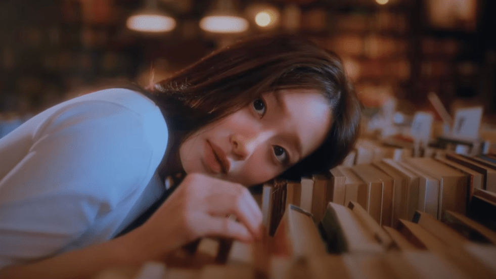 Review do álbum XO, My Cyberlove: cena do MV da title track com Chuu (츄) apoiando a cabeça em cima de livros