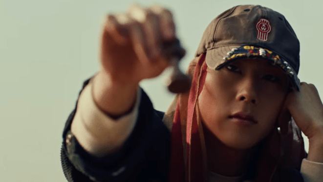 Review do álbum 光 (INSANITY): cena do MV de "STING" com Joohoney (주헌) do Monsta X (몬스타엑스) segurando uma peça de xadrez enquanto olha para a tela