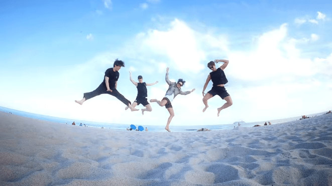 Review do single "growing pains" do Monsta X: cena com quatro dos seis membros na praia, pulando em poses divertidas