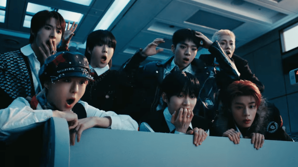 Review do álbum POP IT LIKE do NouerA: cena do MV da title track com Fan, Gihyeon, Hyunjun, Junpyo, Lin, Miraku e Yuseop mostrando expressões de surpresa