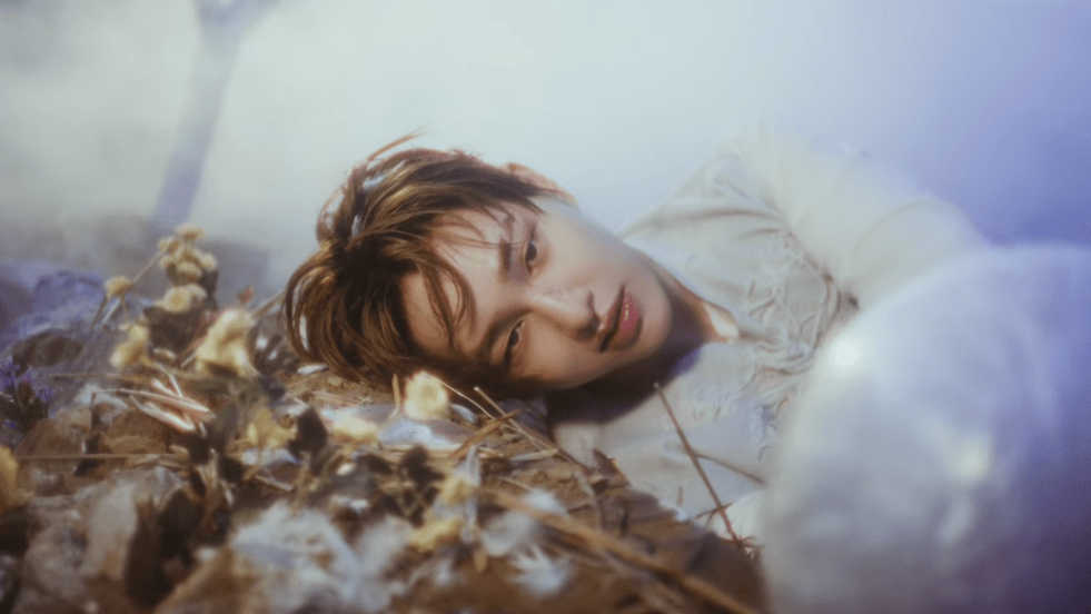 Review do álbum TOUGH LOVE: cena do MV da title track com Onew [SHINee] deitado ao ar livre enquanto olha para um objeto misterioso (um ovo?)