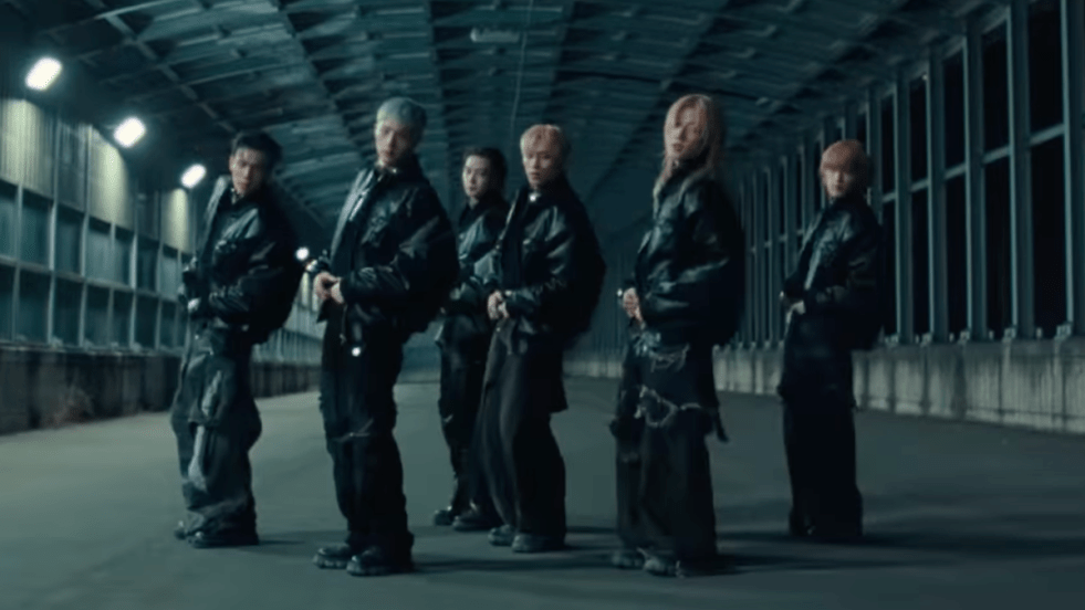 Review do álbum UNIQUE do P1Harmony: cena do MV com Intak, Jiung, Jongseob, Keeho, Soul e Theo vestidos de preto em um galpão