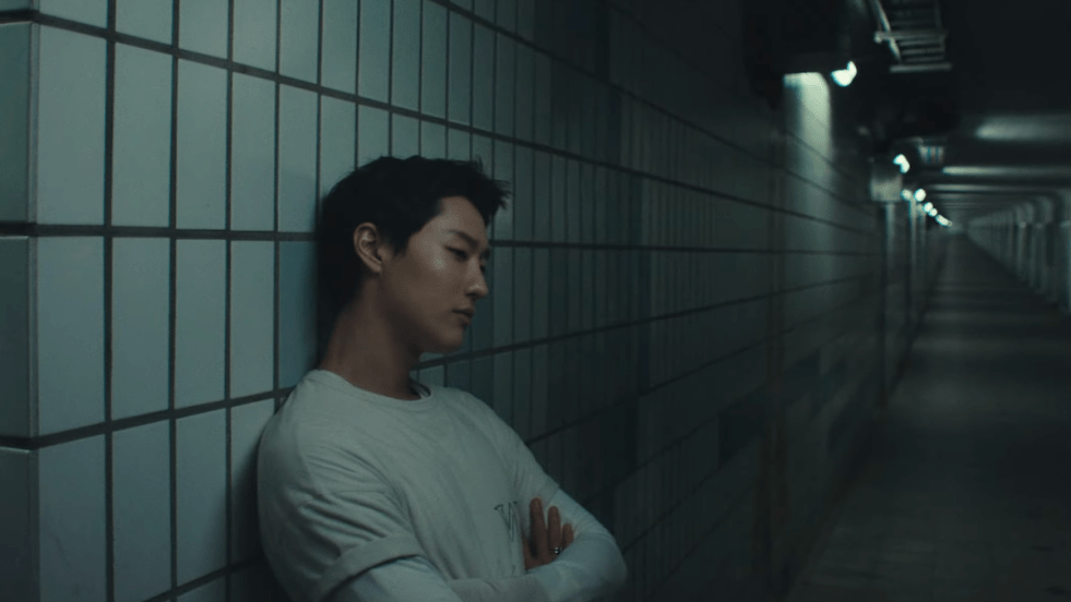 Review do álbum Archive. 1 do WOODZ: cena do MV de "Human Extinction" em um corredor escuro e ele encostado, com os braços cruzados e pensativo, na parede