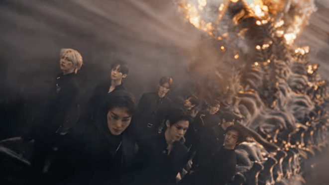 Review do álbum ReDeFINE do CRAVITY: cena inicial do MV de "AWAKE" com todos os membros Allen, Hyeongjun, Jungmo, Minhee, Seongmin, Serim, Taeyoung, Wonjin e Woobin de preto, com fogo ao fundo