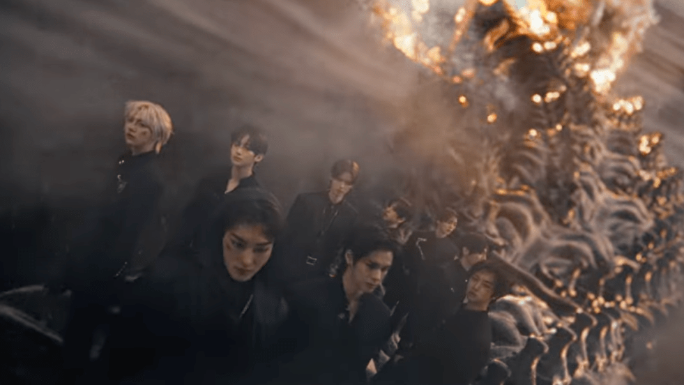 Review do álbum ReDeFINE do CRAVITY: cena inicial do MV de "AWAKE" com todos os membros Allen, Hyeongjun, Jungmo, Minhee, Seongmin, Serim, Taeyoung, Wonjin e Woobin de preto, com fogo ao fundo